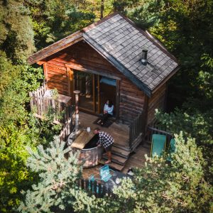 Cabane en bois nichée dans la forêt, avec une terrasse accueillante et un jacuzzi.
