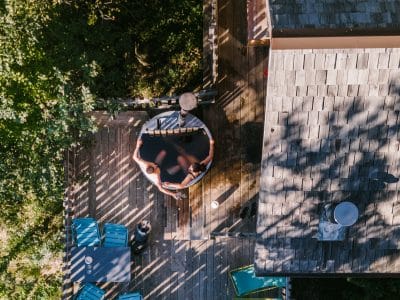 Cabane perchée en bois avec terrasse et jacuzzi, entourée de verdure.