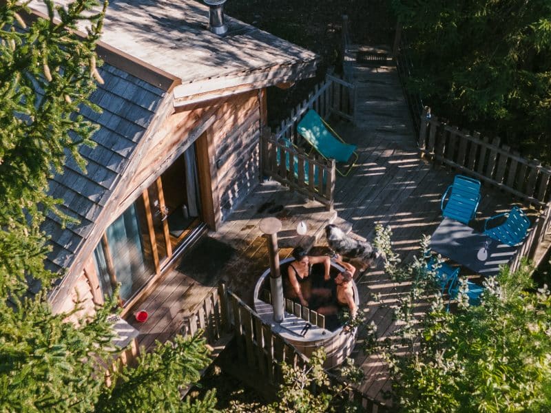 Cabane en bois avec terrasse et jacuzzi, entourée de verdure. Parfait pour se détendre.