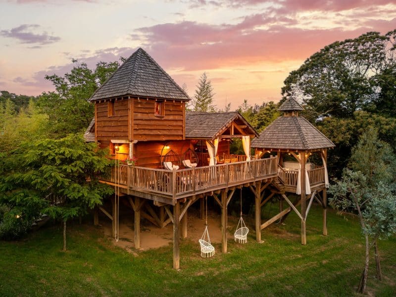 Cabane dans les arbres avec balcons et chaises suspendues au coucher de soleil.