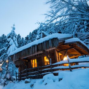 Cabane en bois dans la neige, illuminée par une douce lumière chaleureuse.