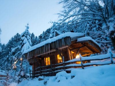 Cabane en bois dans la neige, illuminée par une douce lumière chaleureuse.