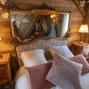 Chalet en bois chaleureux avec lit douillet et miroir ancien, ambiance cosy.