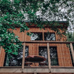 Cabane en bois perchée, entourée de verdure, avec une terrasse accueillante.