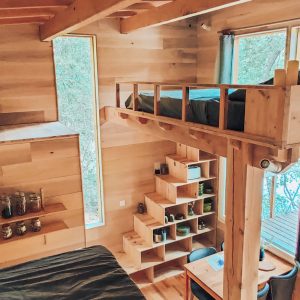Cabane en bois avec mezzanine, grandes fenêtres offrant une vue sur la nature.