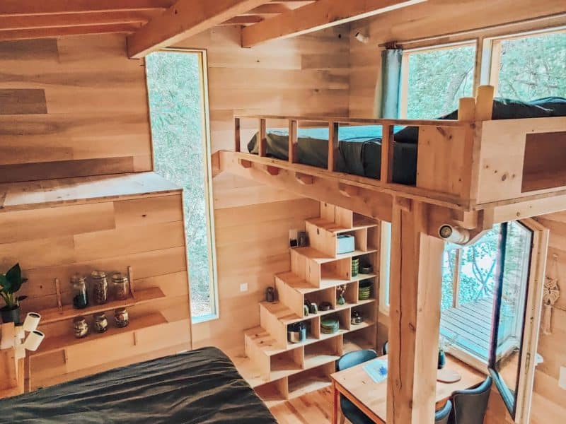Cabane en bois avec mezzanine, grandes fenêtres offrant une vue sur la nature.