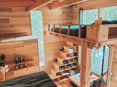 Cabane en bois avec mezzanine, grandes fenêtres offrant une vue sur la nature.