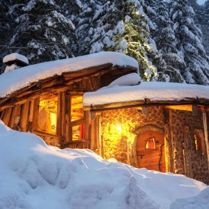 Cabane en bois au cœur de la neige, illuminée par une douce lumière chaleureuse.