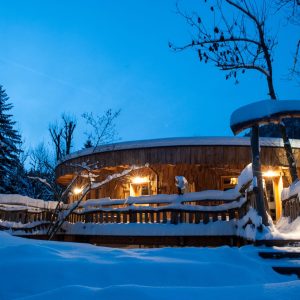 Cabane en bois au bord de la neige, éclairée par des lanternes chaleureuses.