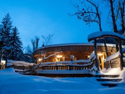 Cabane en bois au bord de la neige, éclairée par des lanternes chaleureuses.