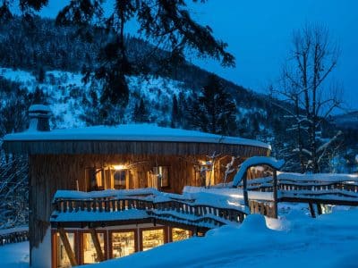 Cabane en bois au cœur de la neige, illuminée par des lumières chaleureuses.
