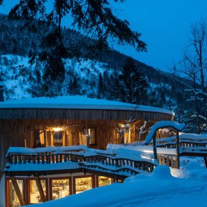 Cabane en bois au cœur de la neige, illuminée par des lumières chaleureuses.