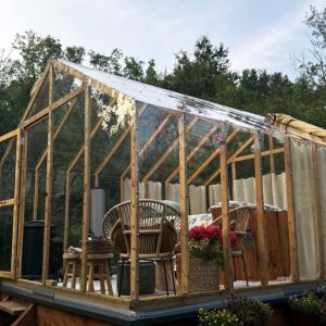 Cabane en verre dans la nature, avec mobilier en rotin et fleurs colorées.