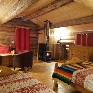 Chalet en bois chaleureux avec cheminée, décor rustique et literie colorée.
