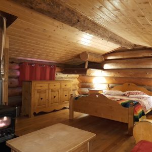 Chalet en bois chaleureux avec lit douillet et poêle à bois, idéal pour un séjour paisible.
