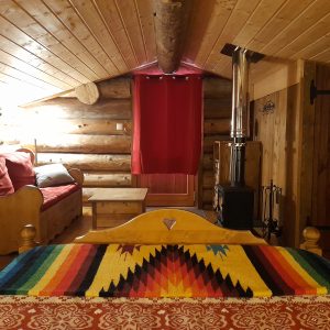 Chalet en bois chaleureux avec lit coloré et poêle à bois, ambiance cosy.
