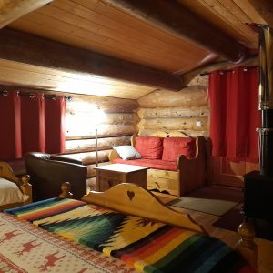 Cabane en bois chaleureuse avec un intérieur en rondins et des rideaux rouges.