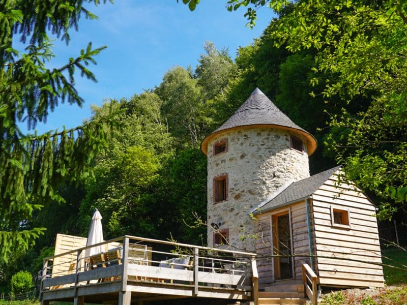 Charmante maison en pierre avec terrasse en bois, entourée de verdure.