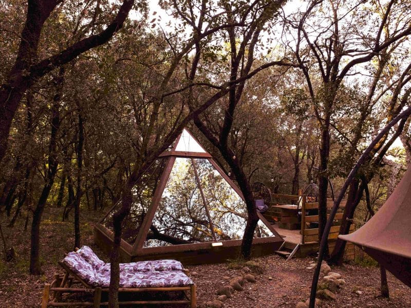 Tente pyramidale en bois, nichée dans une forêt verdoyante du Languedoc-Roussillon.