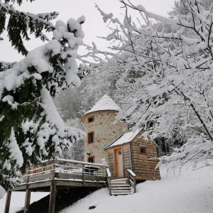 Cabane en bois en forme de tour, entourée de neige et de sapins majestueux.