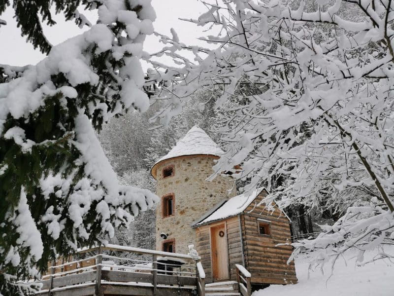 Charmante cabane en bois avec un toit en pointe, entourée de neige et de sapins.