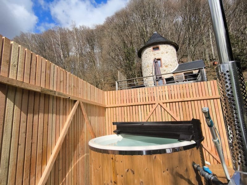 Gîte en pierre avec jacuzzi extérieur, entouré de nature et ciel bleu.