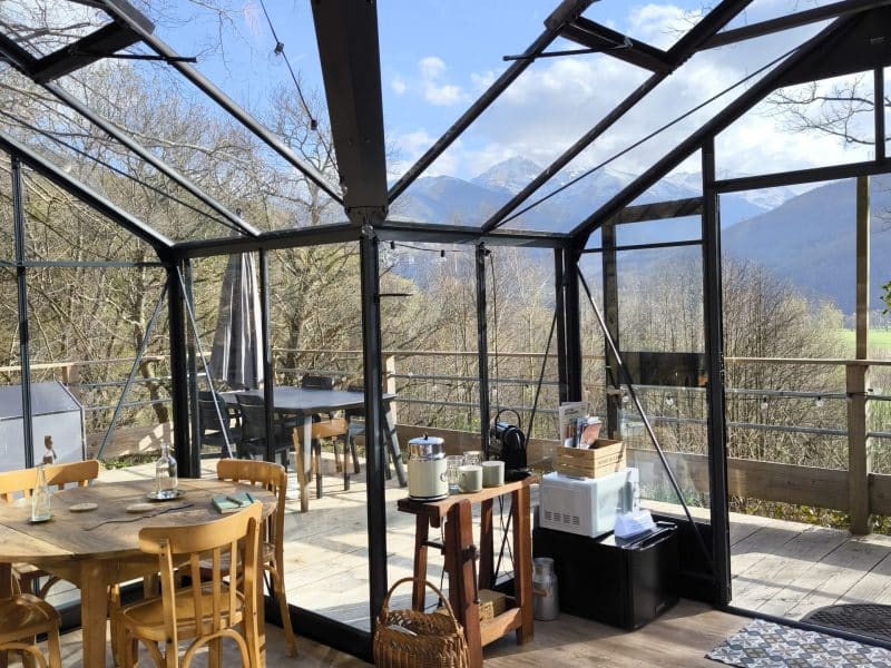 Chalet en verre avec vue montagne, espace lumineux et mobilier en bois chaleureux.