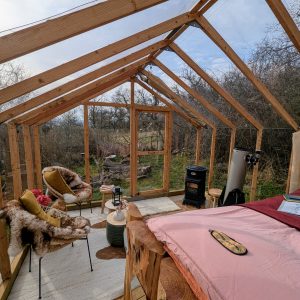 Cabane en bois avec vue sur la nature, fauteuils confortables et poêle à bois.