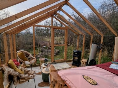 Cabane en bois avec vue sur la nature, fauteuils confortables et poêle à bois.