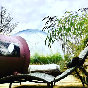 Hébergement insolite en bulle transparente, entouré de verdure et chaises longues.