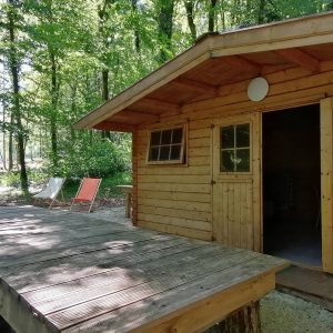 Cabane en bois dans les arbres, entourée de verdure, avec terrasse en bois.