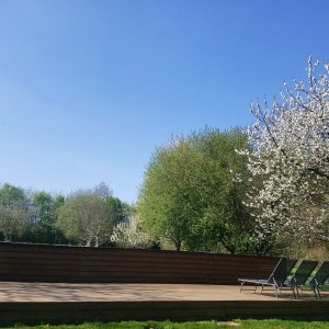 Hébergement insolite en Haute-Normandie avec terrasse en bois et arbres en fleurs.