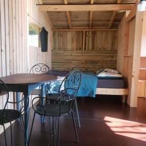 Cabane en bois à Haute-Normandie, avec lit confortable et table en fer forgé.