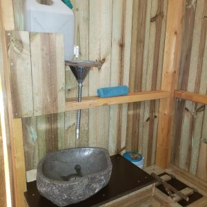 Cabane en bois avec lavabo en pierre, ambiance rustique et naturelle.