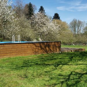 Hébergement insolite en Haute-Normandie avec piscine en bois entourée de vergers fleuris.
