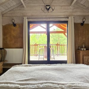 Chalet en bois avec vue sur la nature, lit douillet et terrasse ensoleillée.