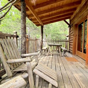 Cabane en bois avec terrasse en bois et chaises rustiques, au cœur de la nature.