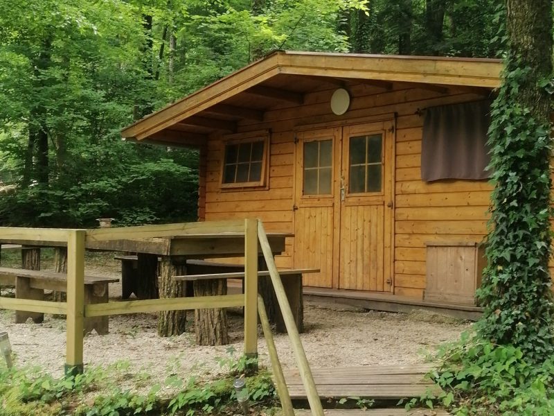 Cabane en bois entourée darbres, avec une terrasse en bois et un coin repas.
