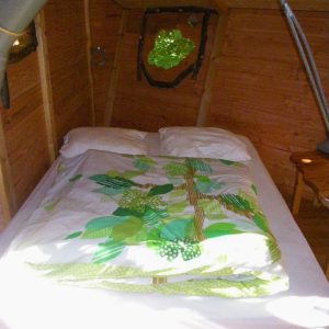 Chambre dans un hébergement en bois, décorée de motifs végétaux et lumineuse grâce à une fenêtre.