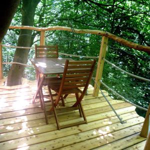 Cabane dans les arbres avec terrasse en bois, entourée de verdure et d'une ambiance paisible.