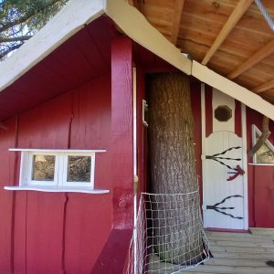 Cabane perchée en bois rouge, intégrée autour dun grand arbre, offrant une vue unique.