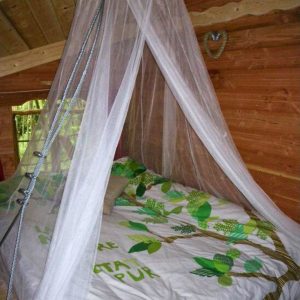 Chambre dans une cabane en bois, lit douillet avec un voile léger et décor végétal.