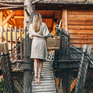 Cabane perchée en bois, accès par un pont suspendu, ambiance naturelle et chaleureuse.