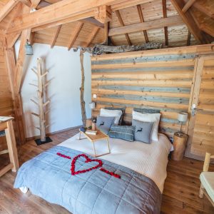 Chalet en bois avec lit décoré dun cœur en pétales, ambiance chaleureuse et cosy.