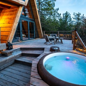 Cabane en bois avec jacuzzi sur une terrasse en bois, entourée de nature.