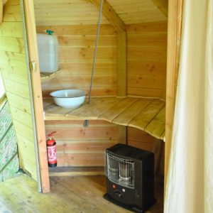 Intérieur d'une cabane en bois avec un lavabo, un poêle et des murs en bois naturel.
