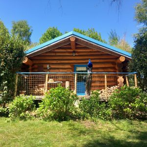 Charmante cabane en bois avec un balcon, entourée de verdure et d'un ciel bleu.