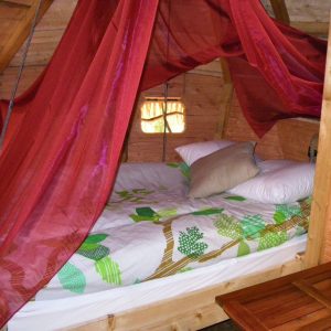 Cabane perchée avec un lit douillet, drapée de voiles rouges et décorée de motifs naturels.