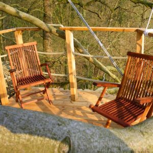 Cabane dans les arbres avec une terrasse en bois et deux chaises confortables.