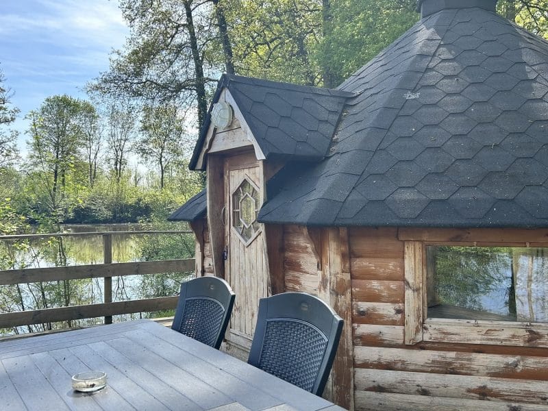 Cabane en bois au bord de leau, avec terrasse et mobilier extérieur.